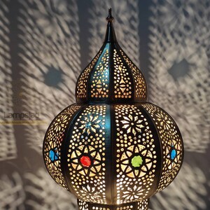 May include: A black metal Moroccan lantern with intricate cut-out designs and colorful glass accents. The lantern has a round body and a pointed top.