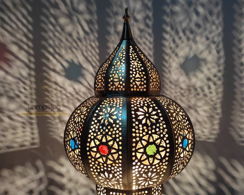 May include: A black metal Moroccan lantern with intricate cut-out designs and colorful glass accents. The lantern has a round body and a pointed top.