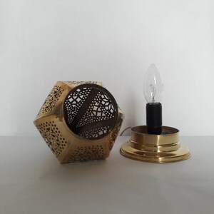 May include: A brass lamp with a geometric, openwork design. The lamp has a single light bulb and a round base.