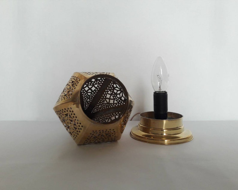 May include: A brass lamp with a geometric, openwork design. The lamp has a single light bulb and a round base.