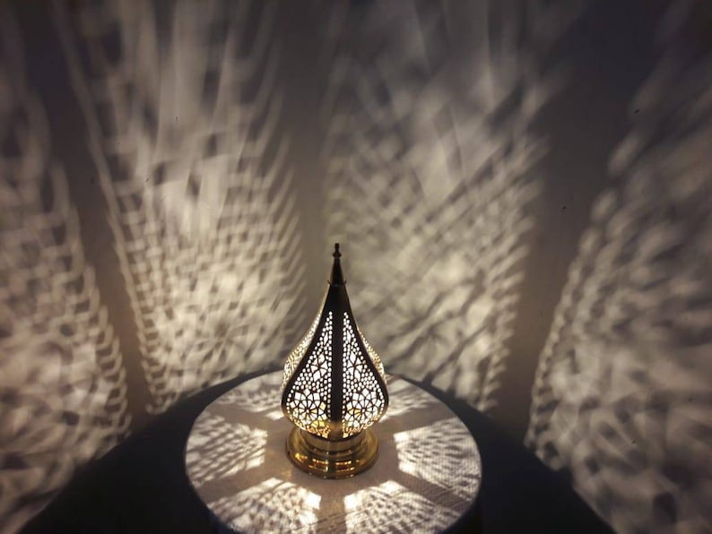 May include: A gold metal table lamp with a geometric design. The lamp is on a table and casting intricate shadows on the surface.