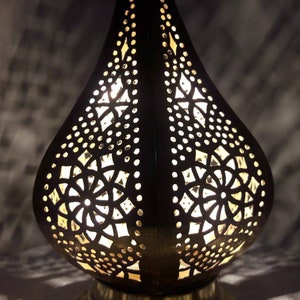 May include: A black metal lamp with intricate cut-out designs in the shape of a teardrop. The lamp is illuminated from within, casting a warm glow through the intricate patterns.