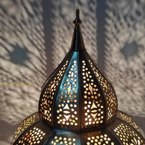 May include: A large, ornate, metal lampshade with a pointed top and intricate cut-out designs. The lampshade is illuminated from within, casting a warm glow.