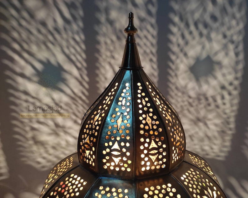 May include: A large, ornate, metal lampshade with a pointed top and intricate cut-out designs. The lampshade is illuminated from within, casting a warm glow.