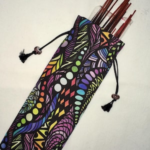 Op de afbeelding: Een kleurrijke stoffen breinaaldenetui met een zwart trekkoord. De etui heeft een levendig patroon van abstracte vormen in verschillende kleuren, waaronder paars, groen, geel en blauw. De etui bevat rode breinaalden.