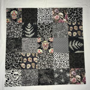 May include: A patchwork quilt featuring a variety of black and white patterns. The quilt includes skull motifs, floral designs, and geometric shapes. The color palette is primarily black, white, and gray, with touches of pink and green.