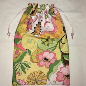 May include: A fabric drawstring pouch featuring a vibrant floral pattern with yellow, pink, green, and brown colors. The bag has a gathered top closure with thin pink cords on both sides, finished with small pink beads at the ends of the strings.