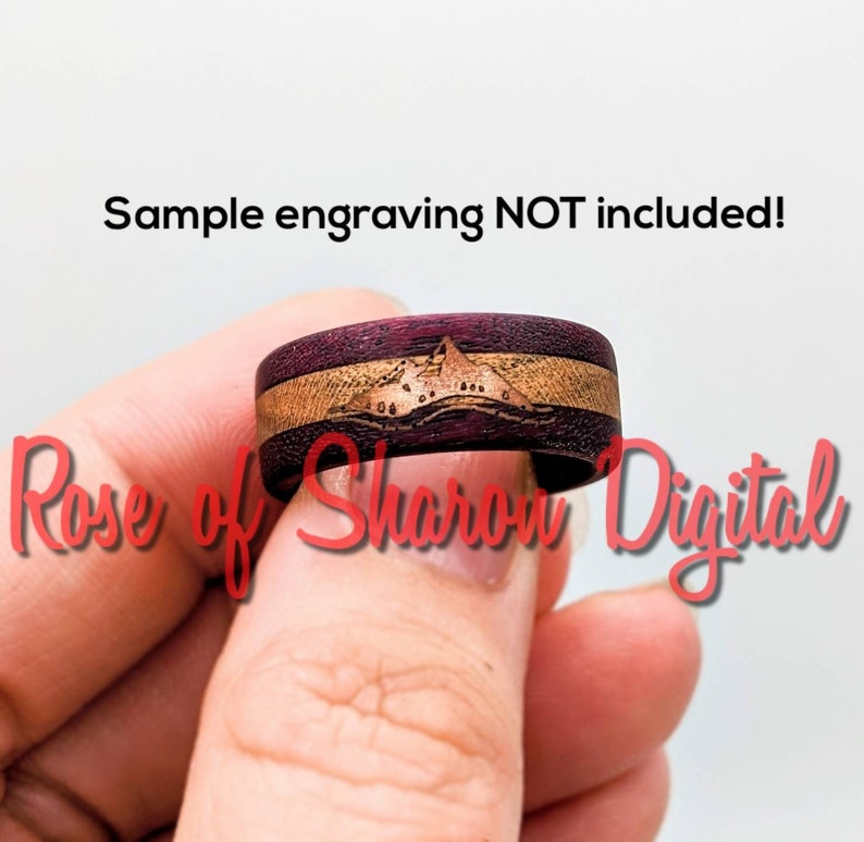 May include: A close-up of a wooden ring with a purple and brown wood grain pattern. The ring has a mountain scene engraved on it. The text "Sample engraving NOT included!" is visible at the top of the image.