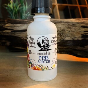 May include: A frosted glass bottle of Pine Scotch essential oil with a black dropper. The label features a wolf logo, floral accents, and the text "High Quality" and "one ounce".