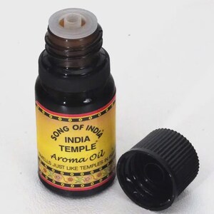 May include: Aroma oil bottle with a black cap. The bottle is dark brown with a yellow label featuring the text "SONG OF INDIA INDIA TEMPLE Aroma Oil". The cap is off to the side.