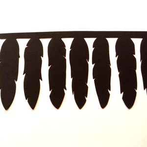 May include: Black feather cutouts attached to a horizontal bar. The feathers are evenly spaced and have a detailed, realistic shape. The background is plain white.