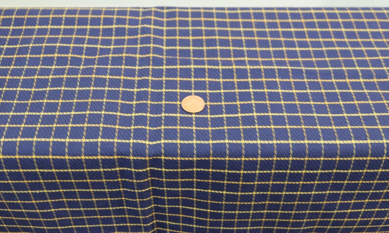 May include: A close-up of a blue and yellow plaid fabric. The fabric has a woven texture and a subtle sheen.