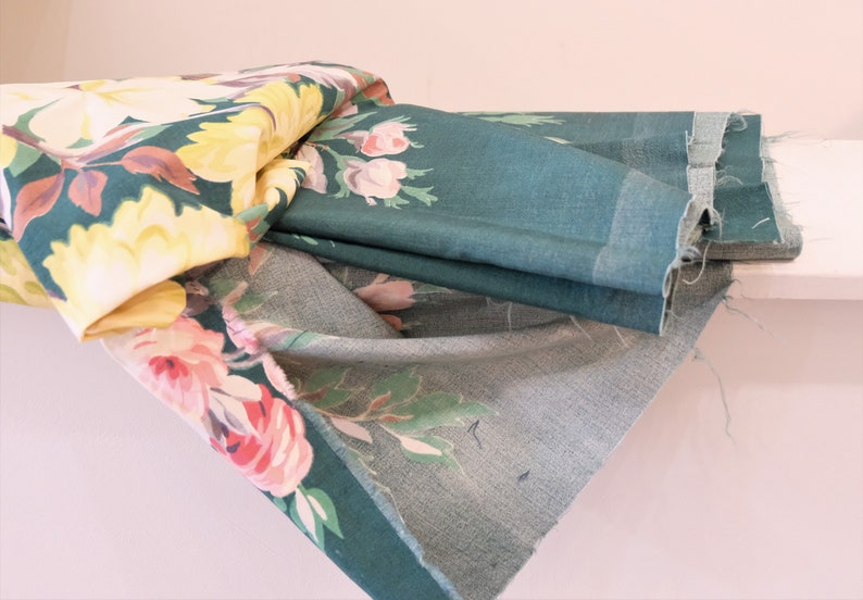 K&ouml;nnte beinhalten: Ein Stapel Stoff mit Blumenmustern in den Farben Rosa, Gelb und Gr&uuml;n. Der Stoff ist gefaltet und &uuml;bereinander gelegt, wobei die oberste Schicht ein dunkelgr&uuml;ner Stoff mit Blumenmuster ist.
