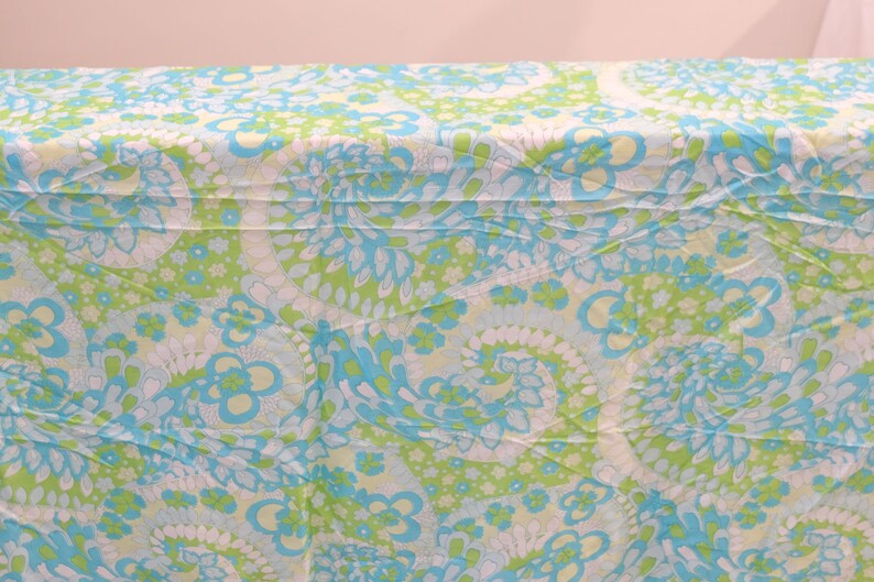 May include: A white fabric with a swirling blue and green floral pattern.