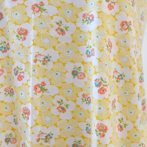 Puede incluir: Tela amarilla con un patr&oacute;n floral blanco. Las flores son peque&ntilde;as y tienen acentos rosados, azules y verdes.