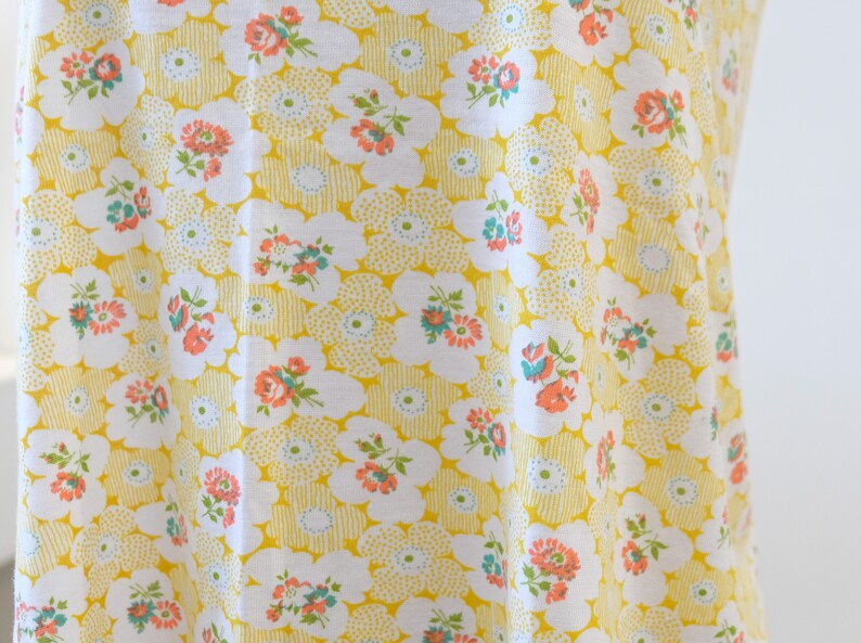 Puede incluir: Tela amarilla con un patr&oacute;n floral blanco. Las flores son peque&ntilde;as y tienen acentos rosados, azules y verdes.