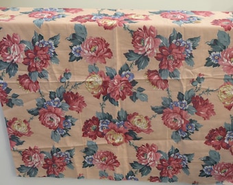 May include: Peach-colored fabric with a repeating floral pattern. The flowers are pink, red, and yellow with green leaves.