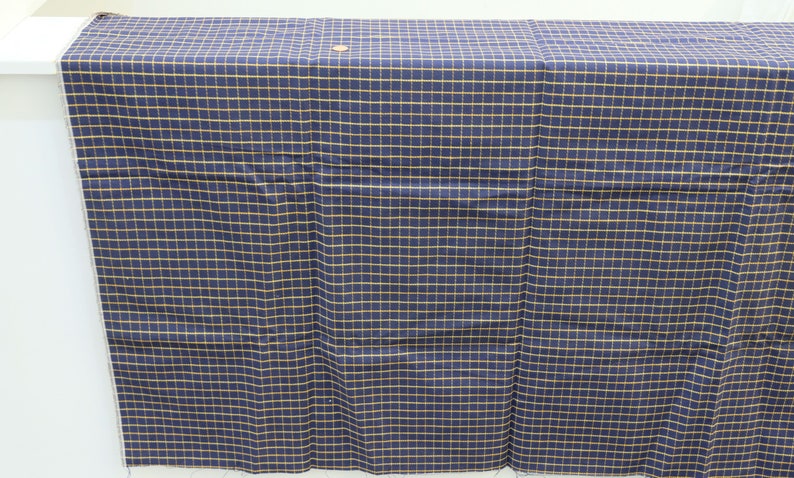 May include: A navy blue fabric with a fine yellow grid pattern. The fabric is folded in half and laid flat on a white surface.