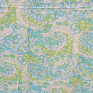May include: A fabric with a repeating pattern of blue, green, and white paisley shapes. The fabric has a crinkled texture.