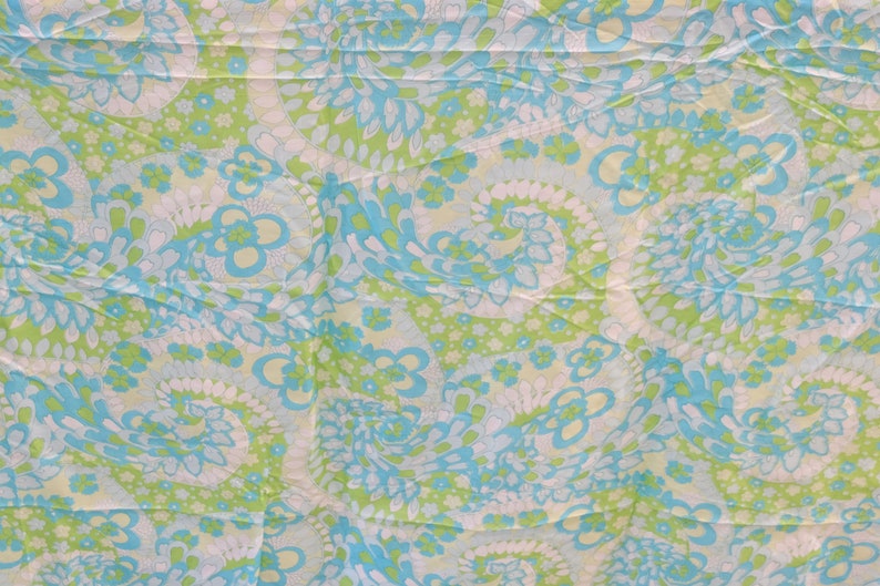 May include: A fabric with a repeating pattern of blue, green, and white paisley shapes. The fabric has a crinkled texture.