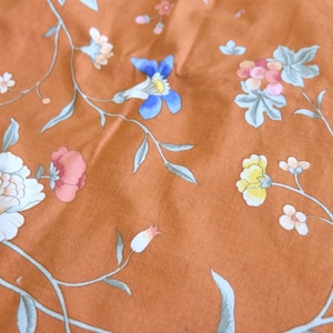 May include: A close-up of a fabric with a floral pattern. The fabric is a light brown color with a variety of flowers in shades of pink, blue, yellow, and white. The flowers are arranged in a repeating pattern on the fabric.