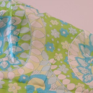 May include: A green fabric with a blue and white floral pattern. The fabric has a paisley design with a repeating pattern of flowers and leaves.