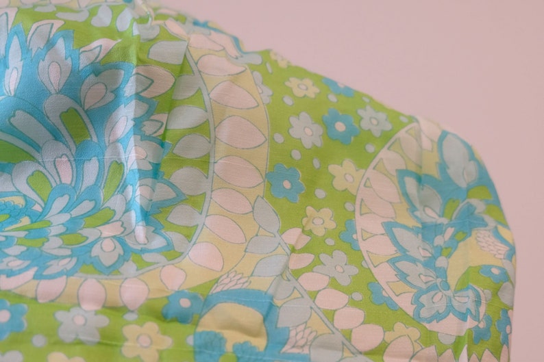 May include: A green fabric with a blue and white floral pattern. The fabric has a paisley design with a repeating pattern of flowers and leaves.