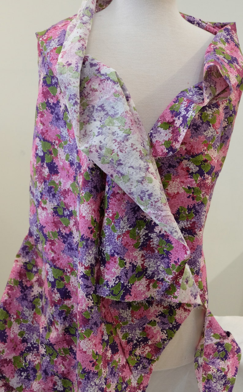 May include: A purple, pink and green floral print fabric with a white background. The fabric is draped over a white mannequin.