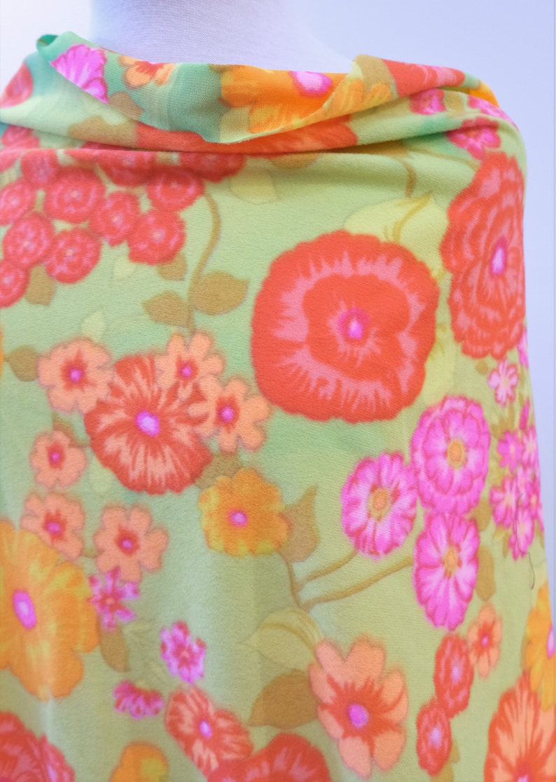 Puede incluir: Una tela verde con un patr&oacute;n floral con flores naranjas, rosas y rojas. La tela tiene una textura suave y transparente.