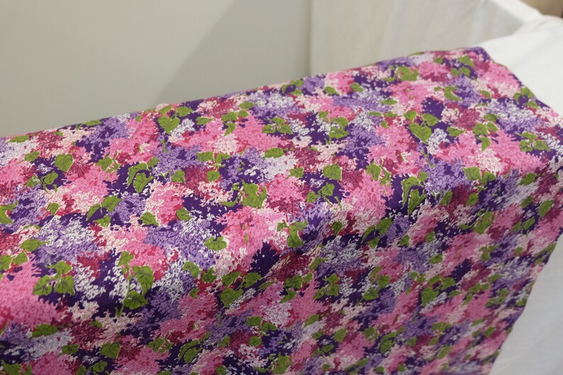 May include: Purple, pink and green floral fabric with a repeating pattern of stylised flowers.