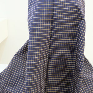 May include: A navy blue fabric with a yellow checkered pattern. The fabric is folded and draped over a mannequin.