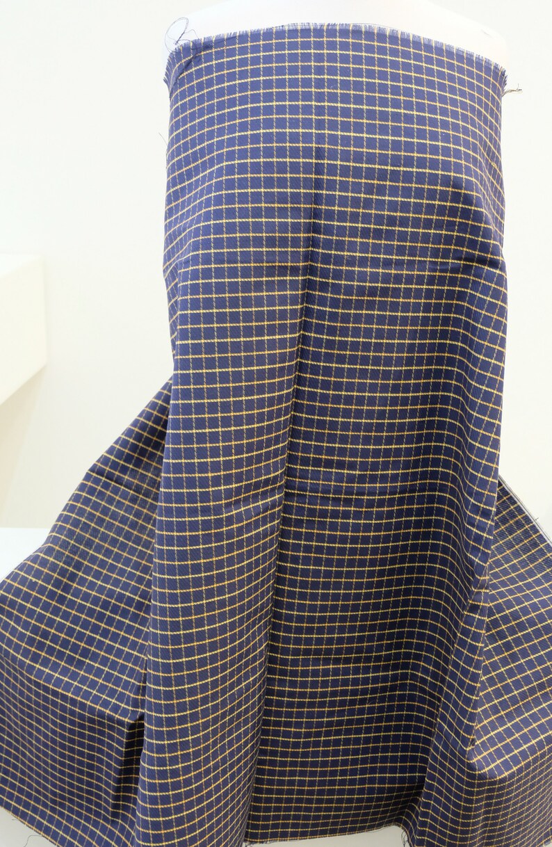 May include: A navy blue fabric with a yellow checkered pattern. The fabric is folded and draped over a mannequin.