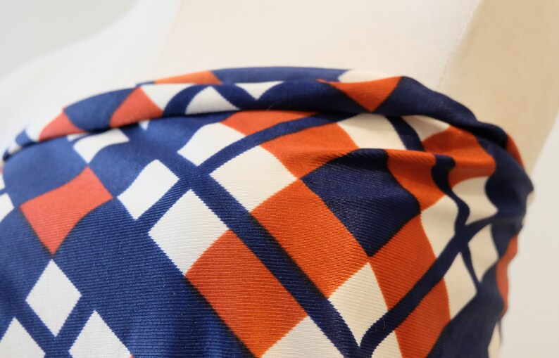 May include: Close-up of a fabric with a geometric pattern in shades of blue, white, and orange. The fabric is folded and has a textured surface.
