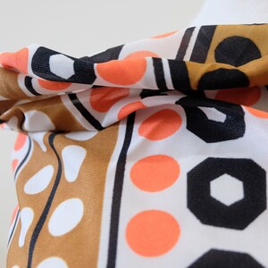 Pu&ograve; includere: Una sciarpa con motivi geometrici e pois, di colore marrone, bianco, nero e arancione.