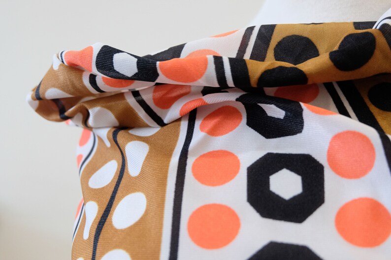 Pu&ograve; includere: Una sciarpa con motivi geometrici e pois, di colore marrone, bianco, nero e arancione.
