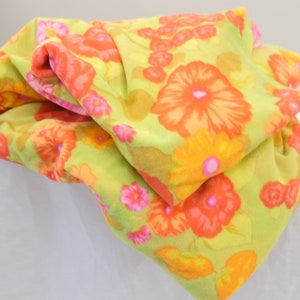 Puede incluir: Una tela verde con un patr&oacute;n floral en tonos naranja, amarillo y rosa. La tela est&aacute; doblada y tiene una textura suave y peluda.