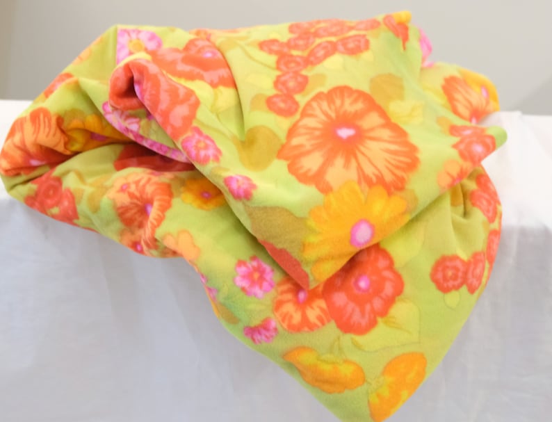 Puede incluir: Una tela verde con un patr&oacute;n floral en tonos naranja, amarillo y rosa. La tela est&aacute; doblada y tiene una textura suave y peluda.