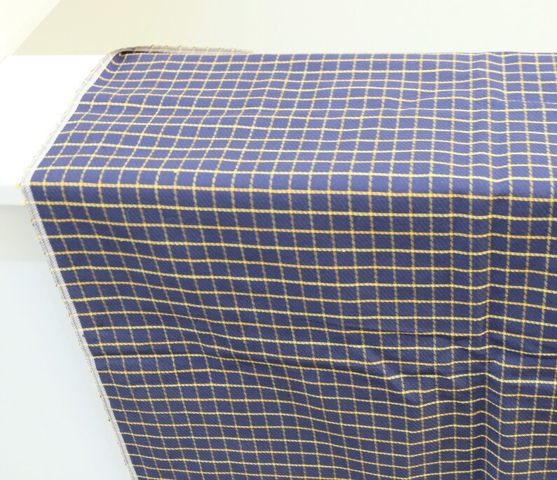 May include: A navy blue fabric with a yellow plaid pattern. The fabric is folded and displayed on a white surface.