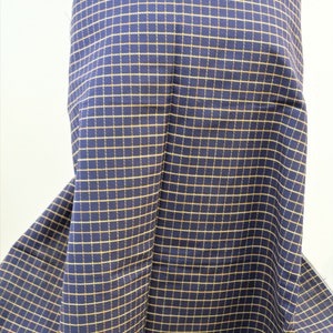 May include: A close-up of a navy blue fabric with a yellow checkered pattern. The fabric is folded and draped over a surface.