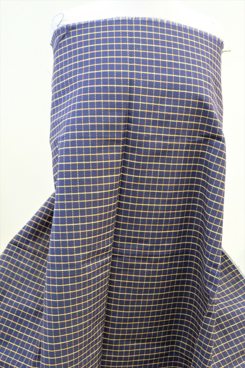 May include: A close-up of a navy blue fabric with a yellow checkered pattern. The fabric is folded and draped over a surface.