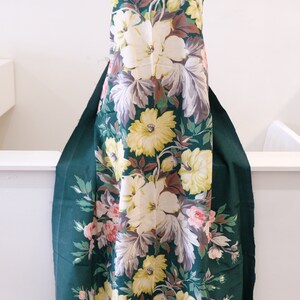 K&ouml;nnte beinhalten: Ein gr&uuml;ner Stoff mit einem gro&szlig;en Blumendruck mit wei&szlig;en, gelben und rosa Bl&uuml;ten. Der Stoff hat einen Vintage-Charakter und w&auml;re perfekt f&uuml;r ein Kleid oder ein anderes Kleidungsst&uuml;ck.