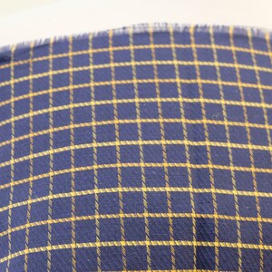 May include: A close-up of a blue and yellow plaid fabric. The fabric has a woven texture and a subtle sheen.