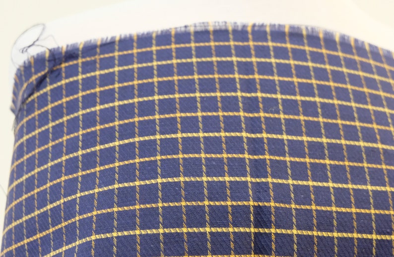 May include: A close-up of a blue and yellow plaid fabric. The fabric has a woven texture and a subtle sheen.