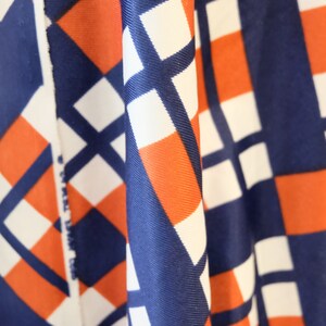 May include: Close-up of fabric with a geometric pattern in shades of blue, white, and orange. The fabric is folded and draped, creating a textured effect.