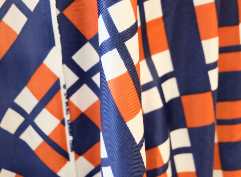 May include: Close-up of fabric with a geometric pattern in shades of blue, white, and orange. The fabric is folded and draped, creating a textured effect.