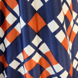 May include: Close-up of a fabric with a geometric pattern in shades of blue, white, and orange. The fabric has a diamond pattern with alternating colors.