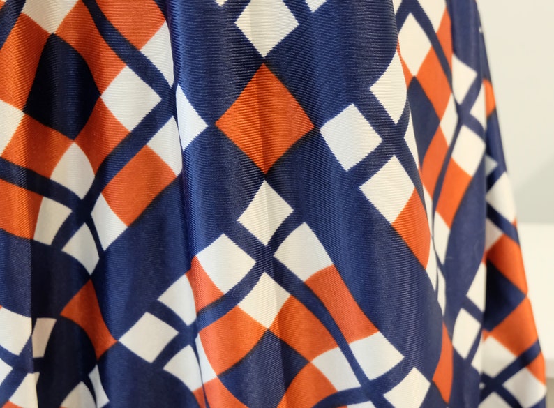 May include: Close-up of a fabric with a geometric pattern in shades of blue, white, and orange. The fabric has a diamond pattern with alternating colors.