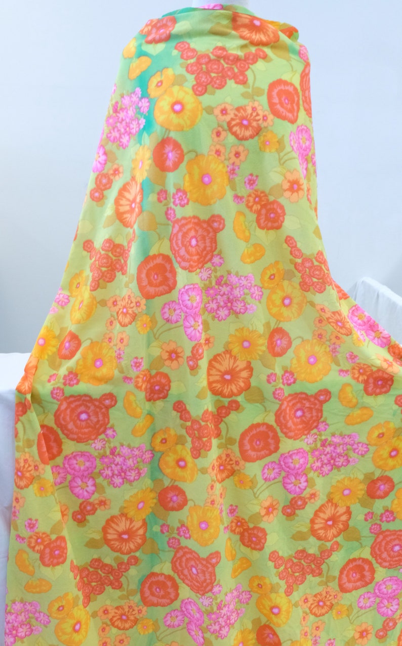 Puede incluir: Tela verde con estampado floral con grandes flores naranjas, amarillas y rosas. La tela tiene un aspecto vintage.
