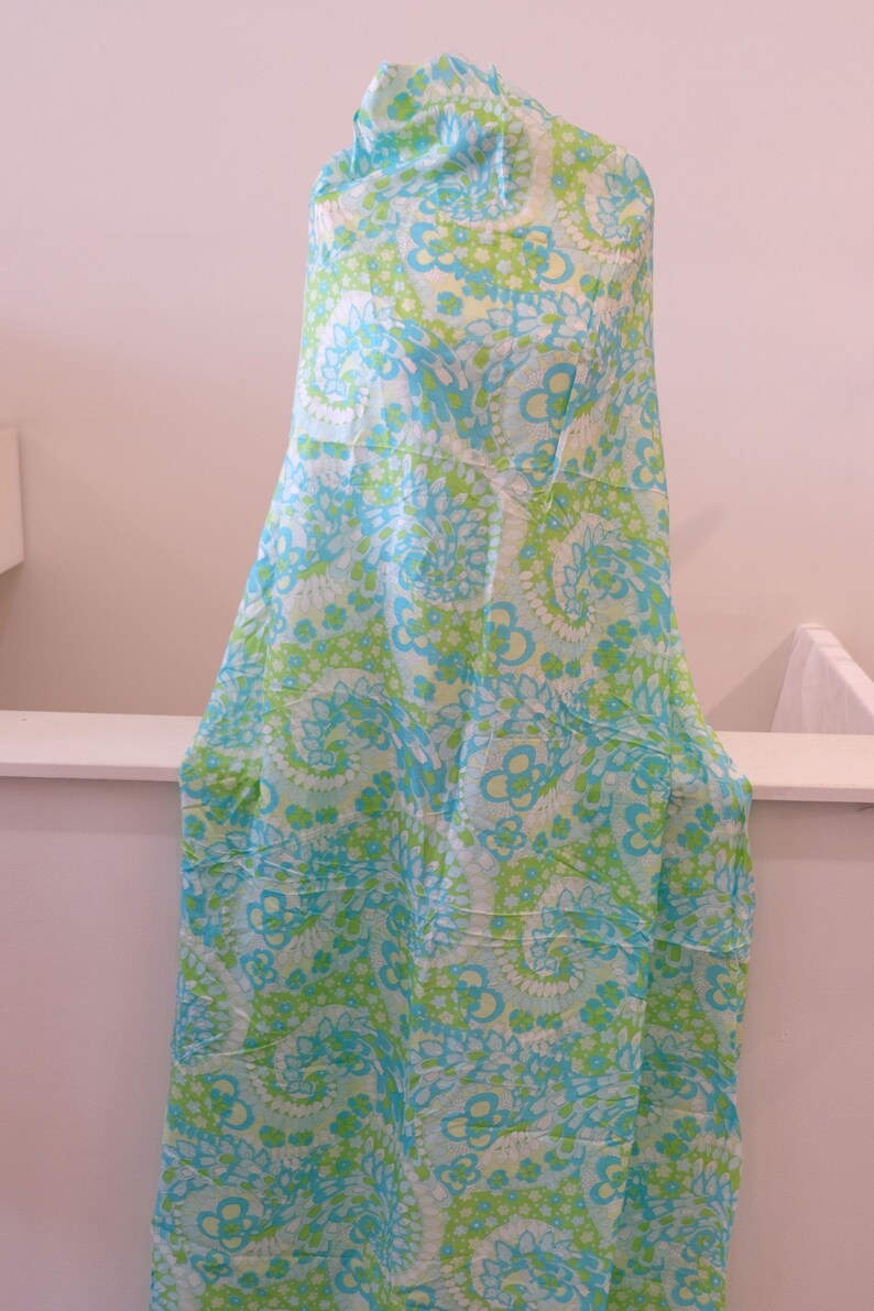 May include: A blue and green fabric with a floral pattern. The fabric is draped over a white surface.