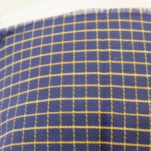 May include: A close-up of a navy blue fabric with a yellow checkered pattern.